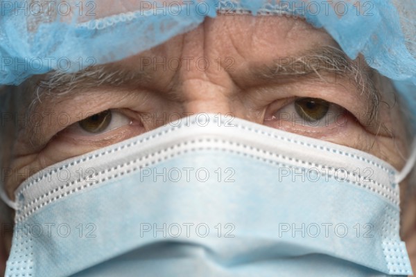 Close up portrait of sad senior adult dressed in surgical face mask with ear straps, covering nose