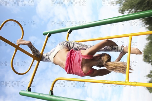 Athletic young blond gymnast working out on colourful metal bars in an outdoor playground hanging
