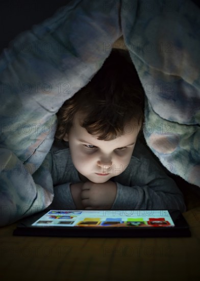 Little girl watching her tablet in the bed. Illuminated child face from device screen. Child