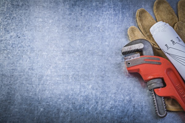 Monkey adjustable wrench protective gloves rolled blueprints on metallic background plumbing