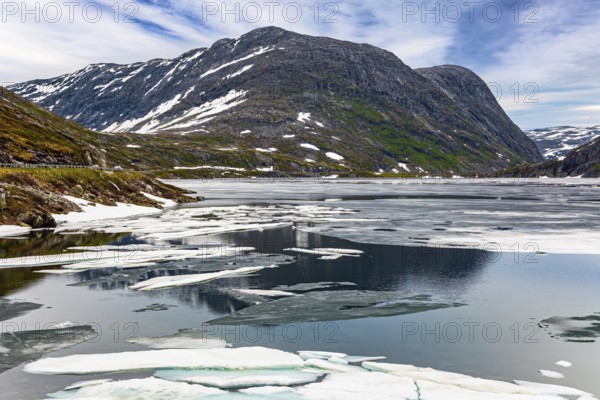Norway. The cold clear water of the lake Djupvatnet is covered with ice in July. The mountains are