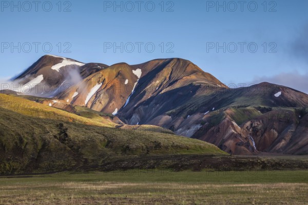 In the hollows of rhyolitic mountain snow. Above the source of hot water steam rises. Early summer