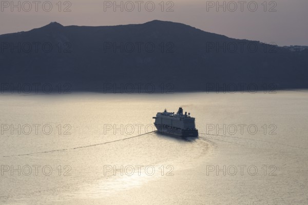 Golden evening light, view from Fira, cruise ship leaving Santorini archipelago, Thirassia island