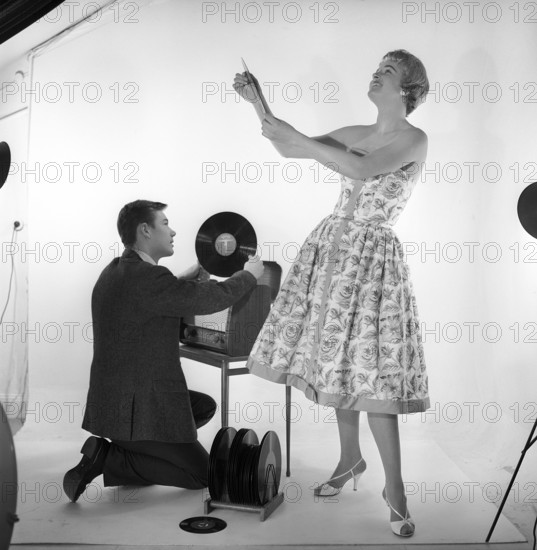 Gramophone in the 1950s. An man is kneeling by a combined recieving set and gramophone cabinet