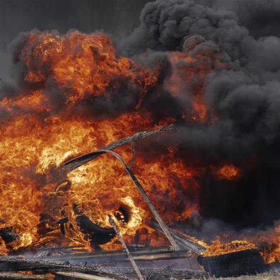 Burning cars tires, strong flame of red-orange fire and clouds of black smoke in sky. Selective
