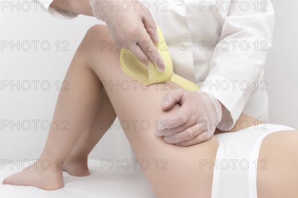 Cosmetologist hands in gloves removing hair on women leg. Depilation procedure with green hot wax