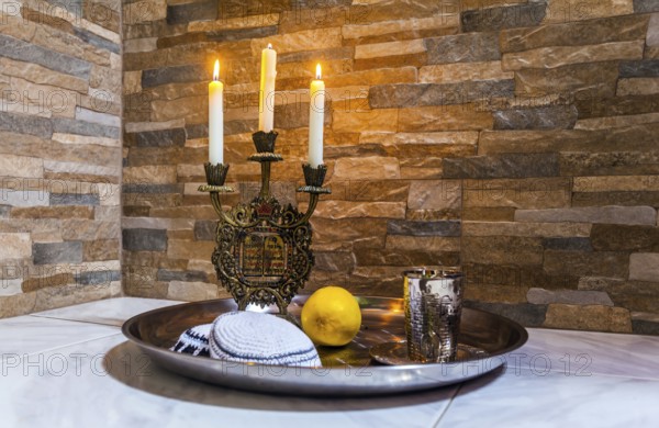 Beautiful candlestick with burning candles, a silver glass for blessing and a white yarmulke.