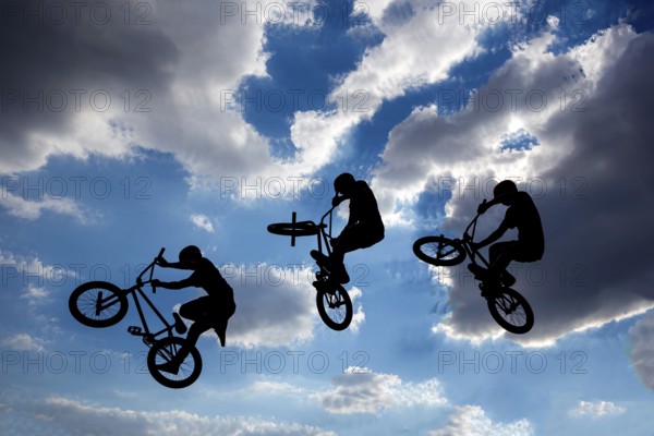 An extreme rider is making a free style jump from a ramp. The young boy with his bicycle is seen as