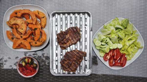 Grilled butternut squash and pork cuts, some fresh vegetable next to it, on glass garden table,