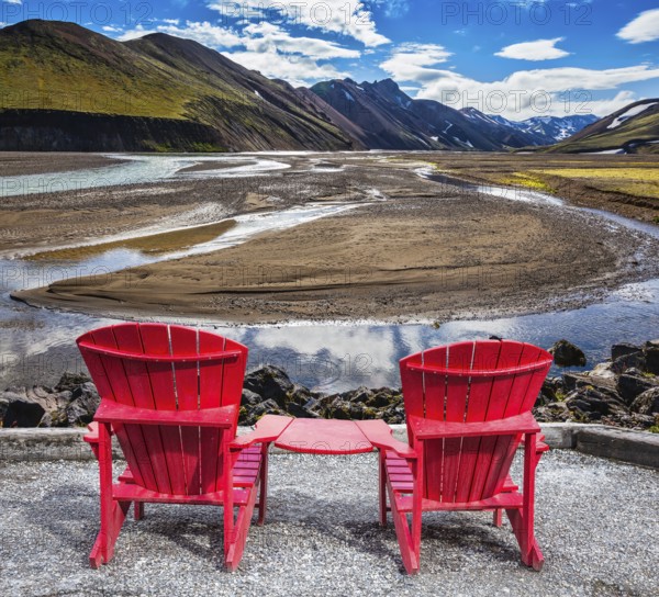 Multi-colored mountains from mineral rhyolite are lit with sun. Two red chaise lounges stand for