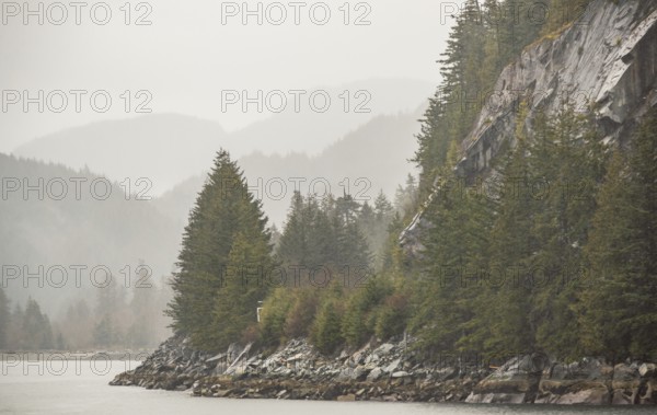 Misty forested mountains and rocky coastline bordering a calm body of water along the Sea to Sky