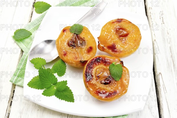 Three halves of quince baked with honey, mint and spoon in a plate on a napkin against a light