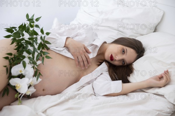 A serene maternity pose featuring natural elements and soft bedding, celebrating the essence of