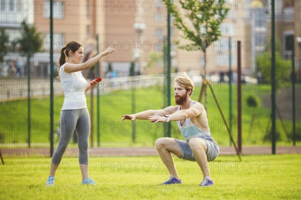 Team work in sports. female trainer training man with beard in park on green grass, lawn at sunset.