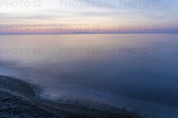 Dawn, cloudy mood in front of sunrise, view from the lava beach to the island of Anafi, long