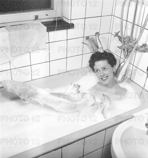 Having a bath 1950. A young smiling woman wearing a princess crown, is having a bath in a bathtub