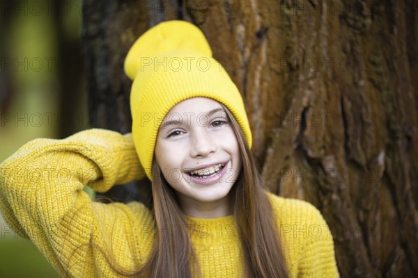 Portrait of modern happy teenage girl with braces dressed in yellow clothes in park. Pretty teenage