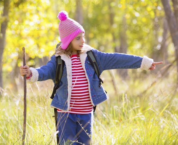 Hiking kid girl with backpack pointing finger in autum poplar trees forest