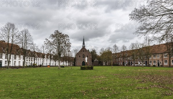 Belgium, 12 08 2018: Old houses and a chapel at the beguinage with bare trees and a meadow during