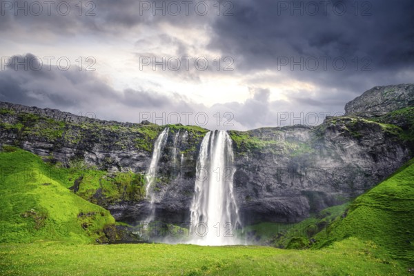 The beautiful Seljalandsfoss waterfall in Iceland surrounded by lava cliffs and green fields in a