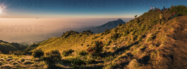 Panoramic photo of mountains surrounding Mount Merbabu and hikers at top during sunrise near Yogya