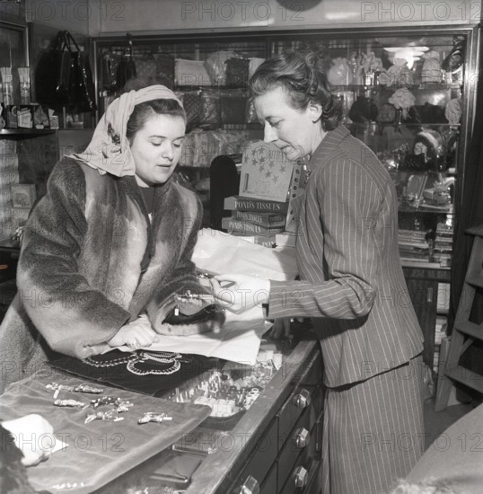 Shopping in the 1940s. A young woman in a store where a sales woman is presenting some of the