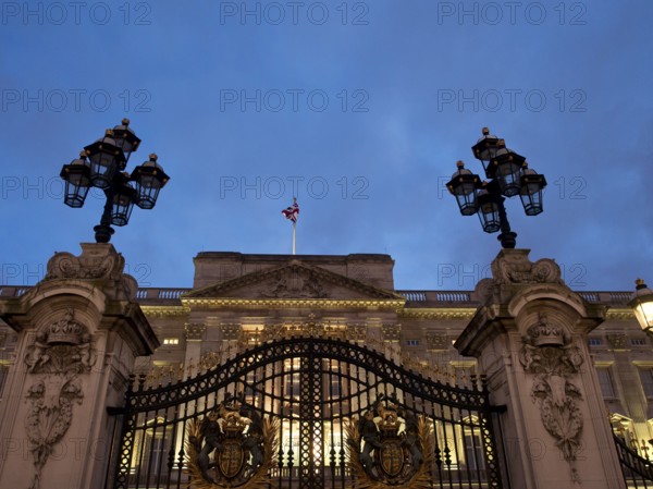 Iron gate with coat of arms and lanterns, illuminated at night in front of a building, London,