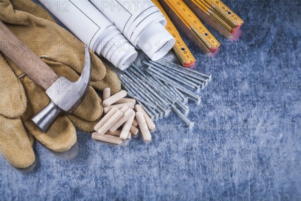 Blueprint rolls claw hammer safety gloves wooden meter metal nails and dowels on scratched metallic