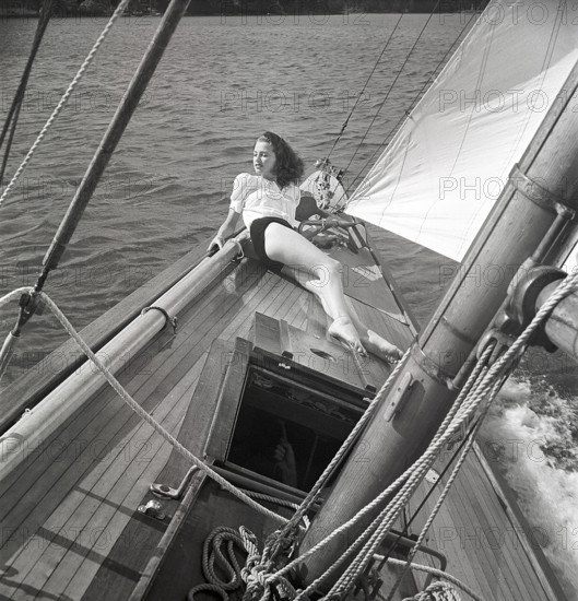 1940s sailing boat. A young woman is aboard a fashionable sailing boat and is lying on deck when it