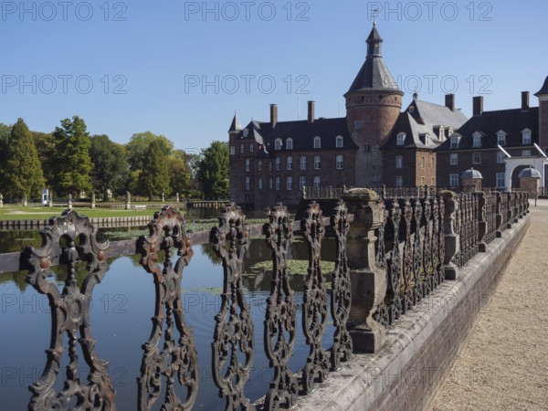 Ornate iron fence along a moat with a view of a brick castle, anholt, isselburg, münsterland,