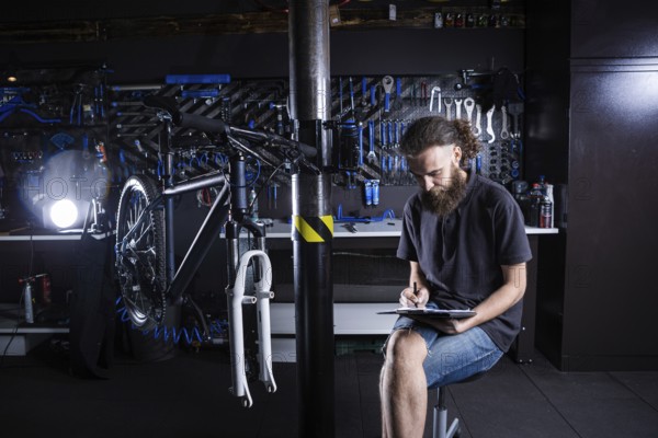 Stylish man with beard, cycle mechanic takes notes, checklist before repairing and servicing bike