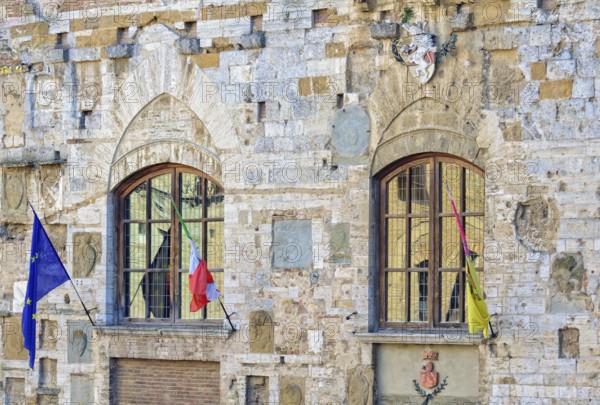 Windows, flags and a coat of arms on the facade of Palazzo Nuovo del Podesta in San Gimignano,