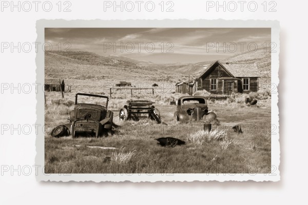Several rusting car wrecks in a meadow in front of a wooden house in the former gold mining town of