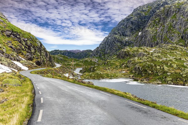 Narrow dangerous mountain road glitters from the rain. The roadside is marked with high poles.