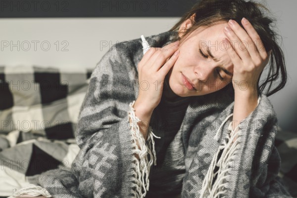Subject disease and treatment. young Caucasian woman sits home bedroom bed wrapped in body blanket