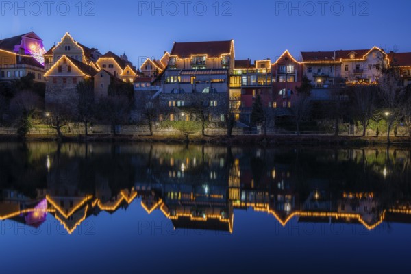 Christmas illuminated house facade of Frohnleiten reflected in the river Mur, blue hour,