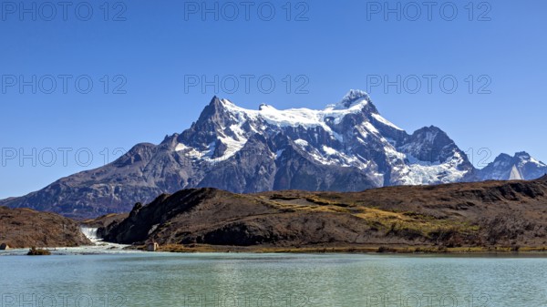 Snowy mountain above a calm river and turquoise water under a blue sky, The landscape of the Torres