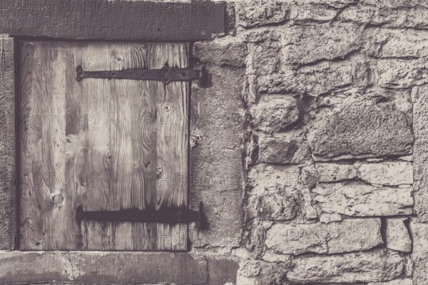 Architectural frame with a weathered wooden trap door and the stone wall, from a traditional german