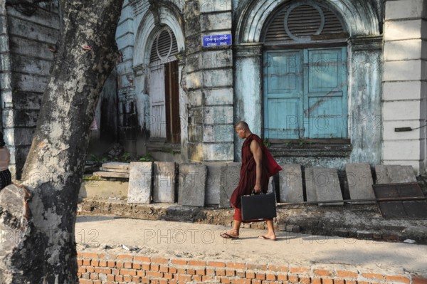 07.10.2013, Yangon, Myanmar, Asia, A Buddhist monk walks with his briefcase past an old colonial