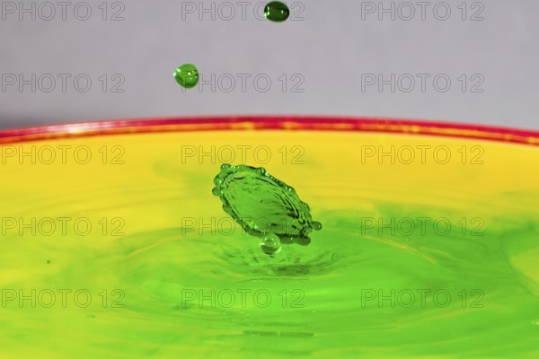 A green drop hits a yellow-green liquid and creates colourful patterns, water droplets, collision,