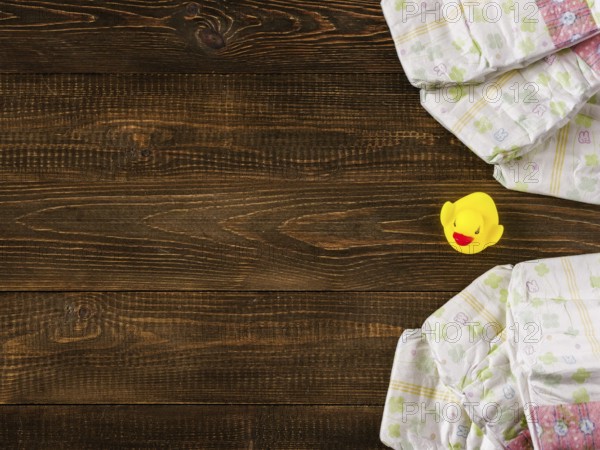 Japanese disposable diapers and the rubber duckling on dark wooden background with copy-space. Flat