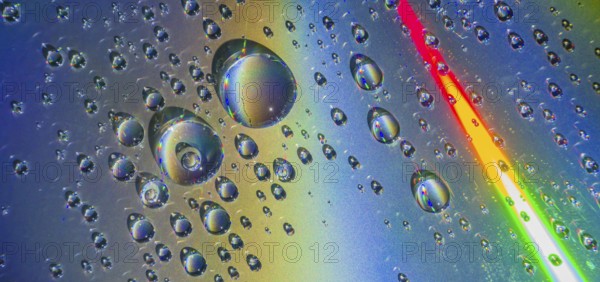 Beautiful closeup of water droplets floating on blueish silver background with rainbow colors