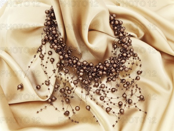 Fashion brown necklace in chaplet shape over golden textile background