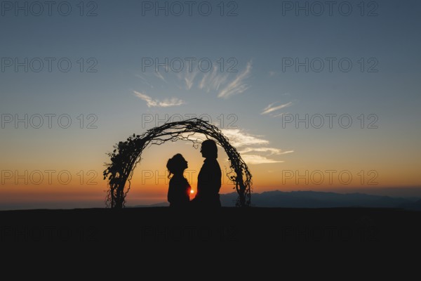 Silhouettes of bride and groom holding hands near the wedding arch at sunset at the wedding
