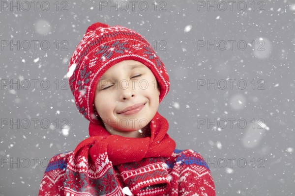 Dreamy child in warm clothing against a winter background. A boy with a red knitted hat and closed
