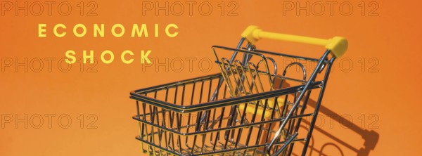 ECONOMIC SHOCK text Empty shopping trolley cart on colorful orange background. Online shopping, buy