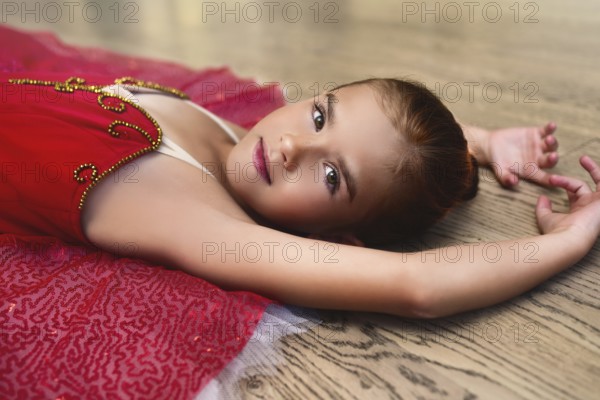 Side view portrait of a cute Beautiful little ballerina in a performance dress lying on the floor