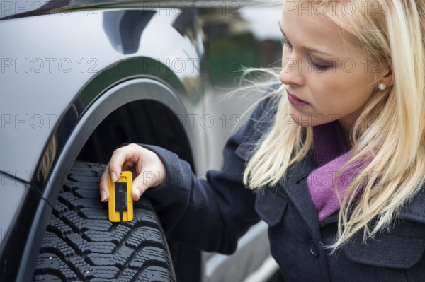 A young woman measures the tread depth of her car tyre. The right depth in the tread of a tyre can