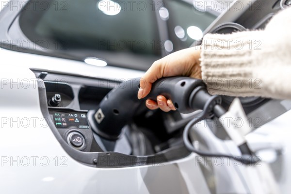 Close up of a hand plugging a charging cable into an electric vehicle at a car dealership,