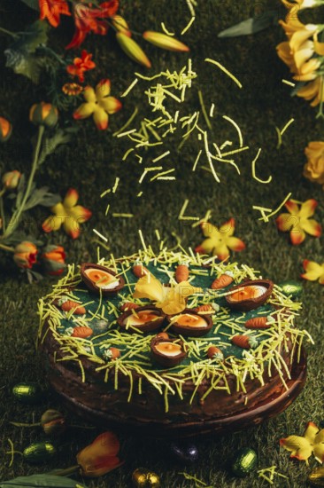 Easter grass falls on Easter cake with carrots and chocolate eggs surrounded by flowers in green